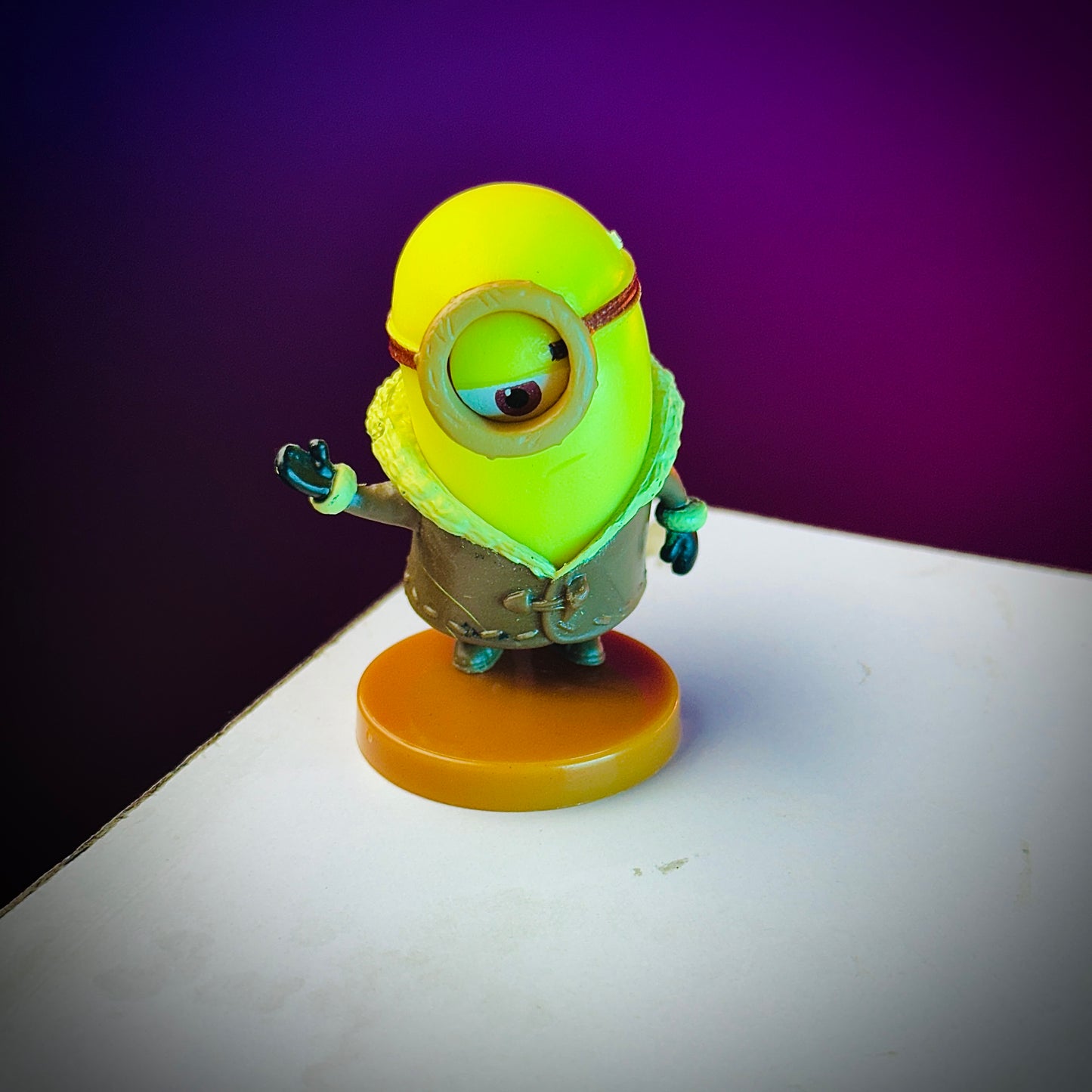 Toy figure of a character with a yellow head and brown body on a purple and white background