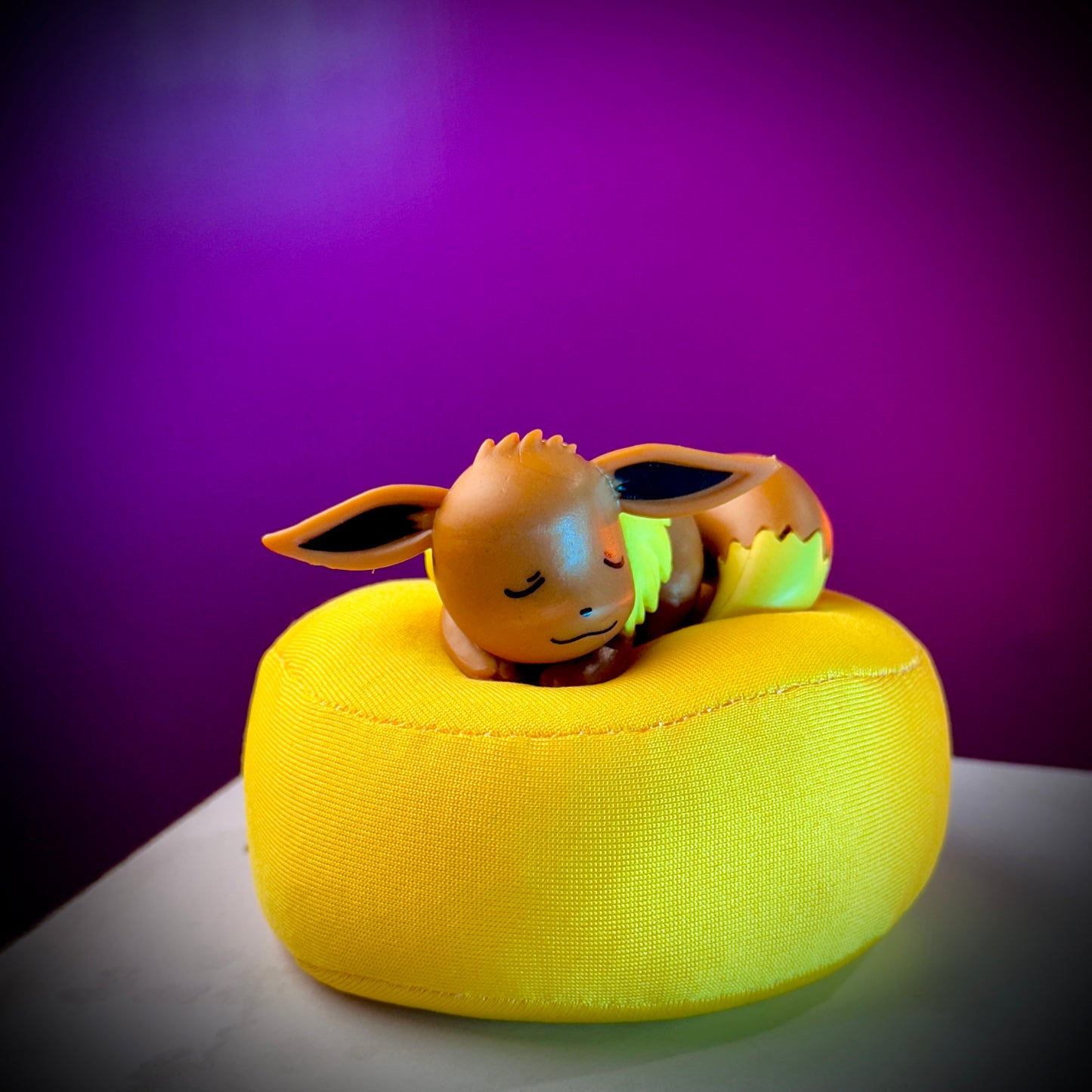 Small figurine of a creature on a yellow cushion with a purple background
