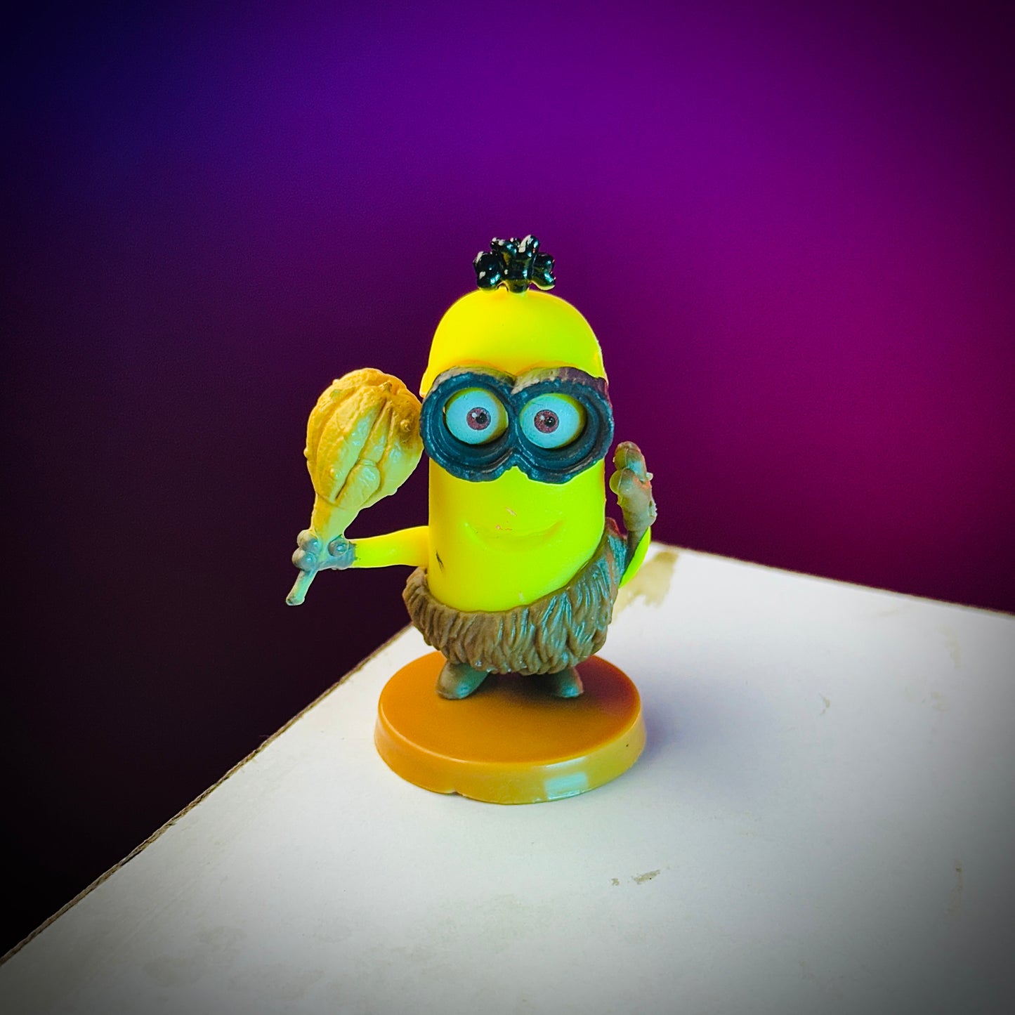 Toy figure of a character in a yellow hat and blue goggles holding a leaf on a purple background