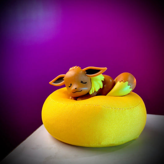 Small figurine of a creature on a yellow cushion with a purple background