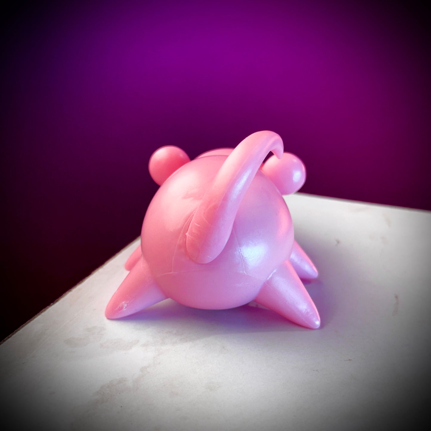 Pink ceramic teapot on a white surface with a purple background